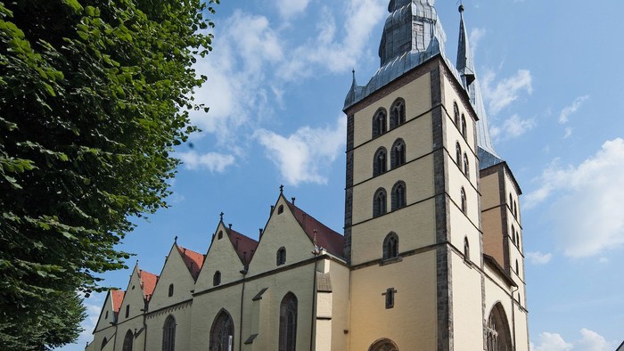 Große Kirche mit hohem Turm und spitzen Dachformen vor blauem Himmel