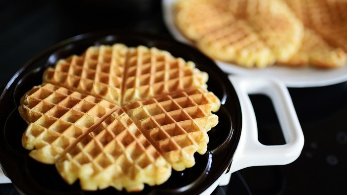 Ein Waffeleisen mit goldbraunen Waffeln und ein Teller mit weiteren Waffeln daneben.