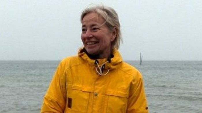 En kvinde i gult regnjakke står ved havet med en lighthouse i baggrunden