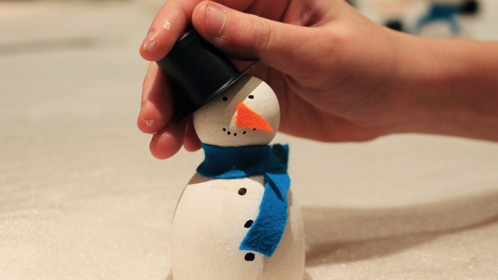 Eine Hand setzt eine schwarze Mütze auf eine Schneemannfigur.