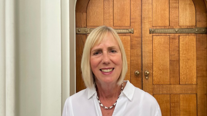 En kvinde med blond hår står foran en trædør.