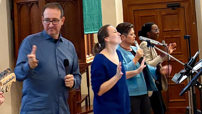Vier Personen singen mit Mikrofonen in einem Raum.