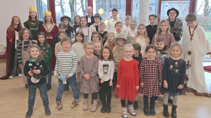 Eine Gruppe von Kindern und Erwachsenen posiert in festlicher Kleidung für ein Gruppenfoto in einem Raum.