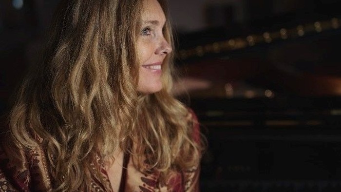 En kvinde med lang, blond hår sitter ved et piano i en koncertsal.