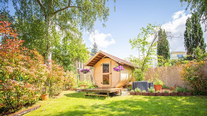 Ein kleines Holzhäuschen in einem üppigen Garten mit verschiedenen Pflanzen und Bäumen.