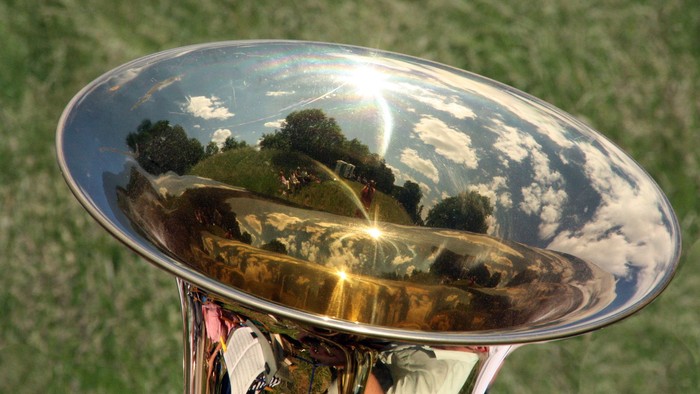 Der Himmel und Bäume spiegeln sich in einem Metallinstrument wider.