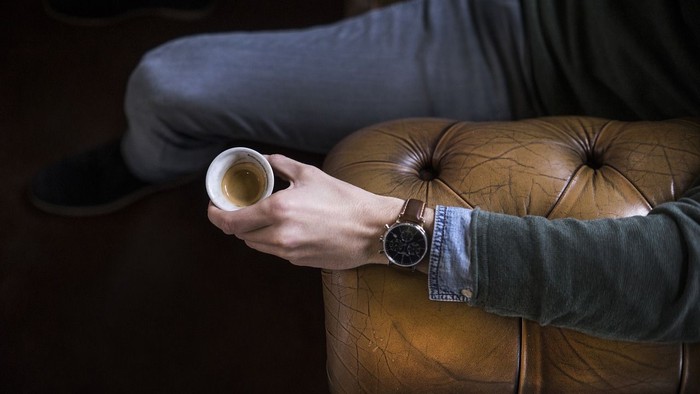 En person sidder på en brune læderstol og holder en kaffe.