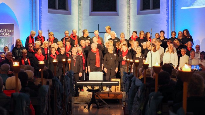 Ein großer gemischter Chor vor dem Altar in einer in blaues Licht gehüllten Kirche, gesehen aus dem Publikum im Mittelgang 