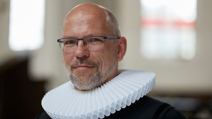 Mann mit Glatze und Kragen, trägt Brille, lächelt