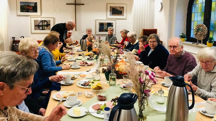 Man sieht viele Menschen beim gemütlichen frühstück an einem reichhaltig gedeckten Tisch.
