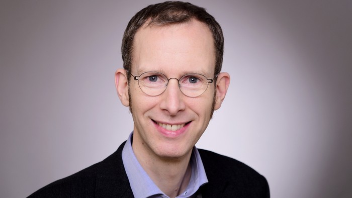 Mann mit Brille und Anzug lächelt in die Kamera.