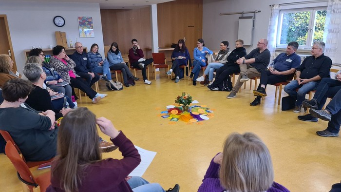 Gruppe von Menschen, die im Kreis sitzen und sich in einer Diskussion oder Besprechung befinden.