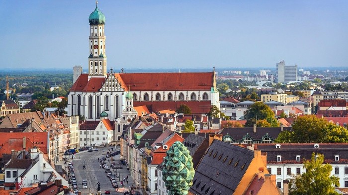 Stadtansicht mit großer Kirche, bunten Dächern und einer grünen Statue.