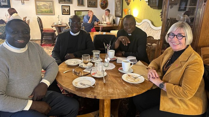 3 Männer und 1 Frau sitzen in einem Cafe an einem gedecktenTisch.