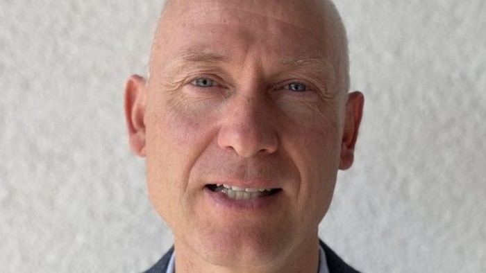 En bald, eldre mand med en mørk jakke og blå skjorte.