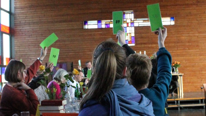 Eine Gruppe von Menschen hält grüne Pappsterne in einem Raum mit Backsteinwänden.
