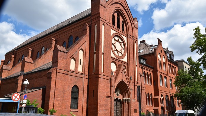 Großes rotes Backsteingebäude mit Rundbogenfenstern und Uhrturm.