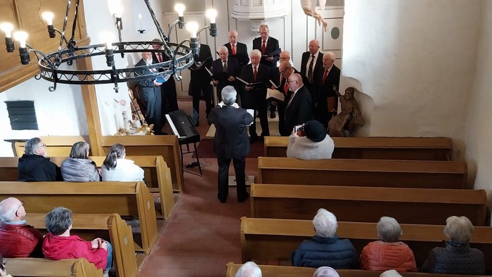 Männer singen im Altarraum. Menschen sitzen in den Bänken. Die Lichterfelder Kirche von der Empore aus.