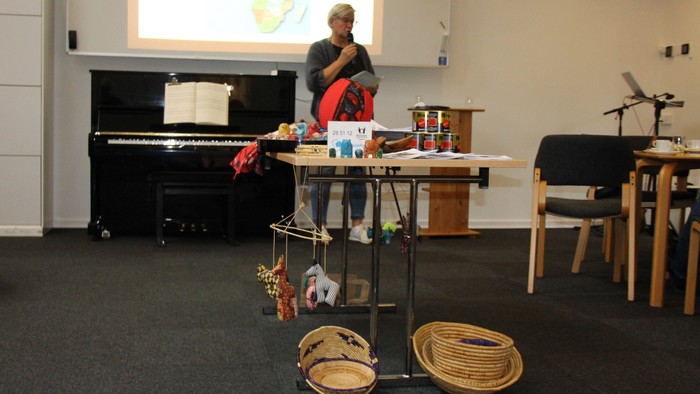 Et bord med afrikanske varer står foran foredragsholderen. Bag ed hende er et kort over Afrika på tavlen