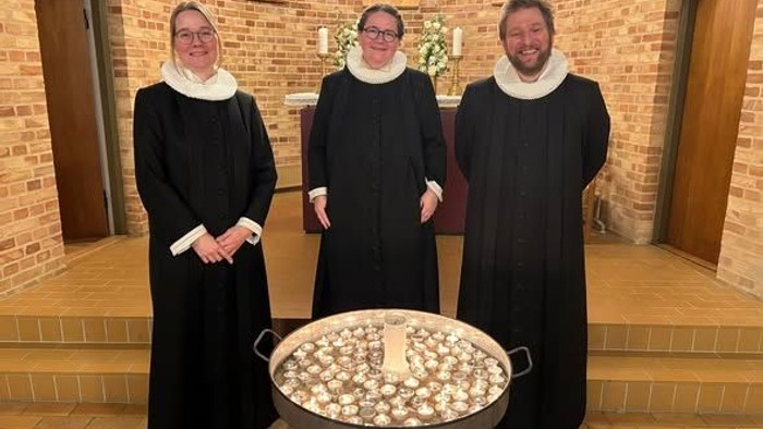 Træ præster stående bag et lysfad med tændte fyrfadslys