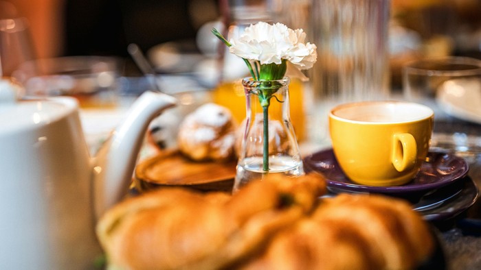 Frühstückstisch mit Pfannkuchen, Kaffee und Blumen.