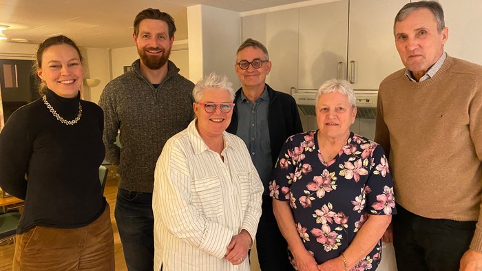 En gruppe af seks personer smiler til kameraet i en køkkenmiljø