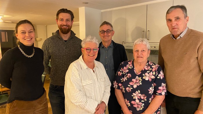 En gruppe af seks personer smiler til kameraet i en køkkenmiljø