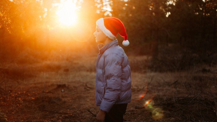 Ein Kind mit einer Weihnachtsmannmütze steht draußen bei Sonnenuntergang.