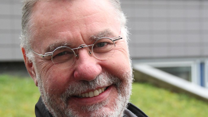 Hans-Peter Naumann ist Pfarrer und unterrichtet Religion an einer Schule. Er trägt eine runde Brille und kurzes, graues Haar und einen kurzen Vollbart. Hans-Peter Naumann lächelt auf dem Bild.