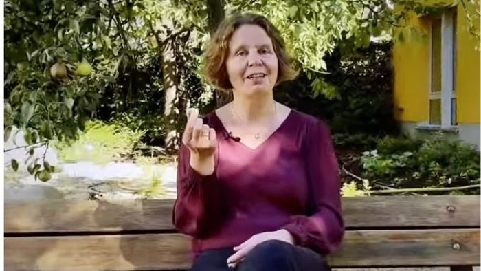 Foto von Pfarrerin Claudia Mieth auf einer Bank sitzende in die Kamera sprechend. In der Hand hält sie einen Stein - ein Souvenir aus dem Urlaub.