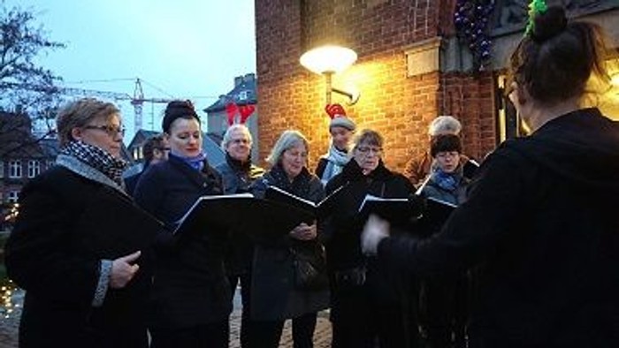 En gruppe af korister synger på gaden med noter i hånden