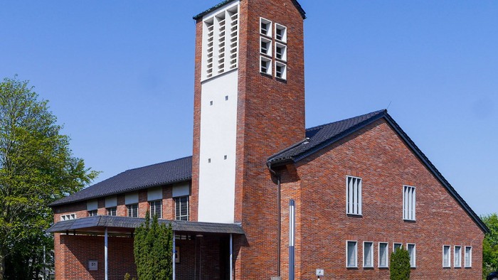 Eine moderne Backsteinkirche mit einem auf einer Seite weiß gestrichenen Turm vor blauem Himmel.