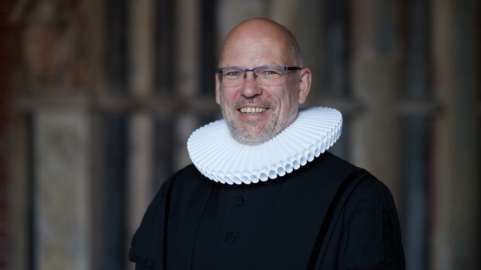 Mann in historical Kleidung mit Kragen und Brille lächelt