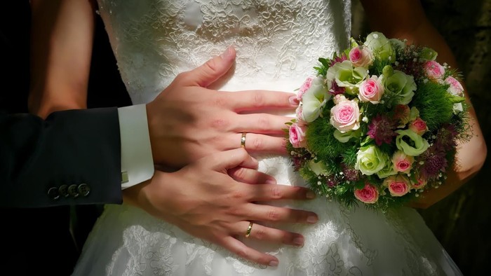 Ein Paar, das sich an den Händen hält, die Braut mit Brautstrauß, Hochzeitskleidung sichtbar.