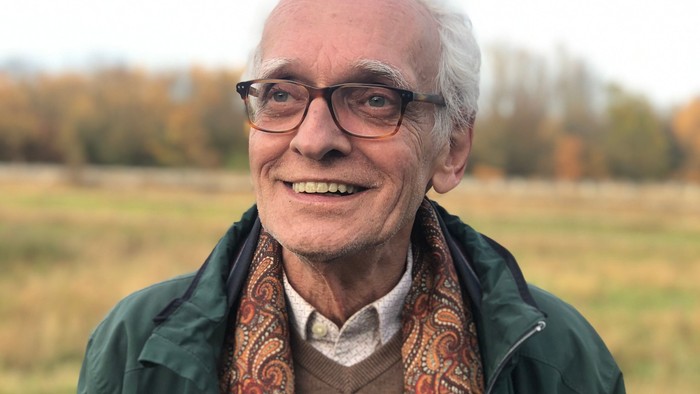 Lächelnder älterer Mann in einer Outdoor-Umgebung mit Brille, Jacke und gemustertem Schal.