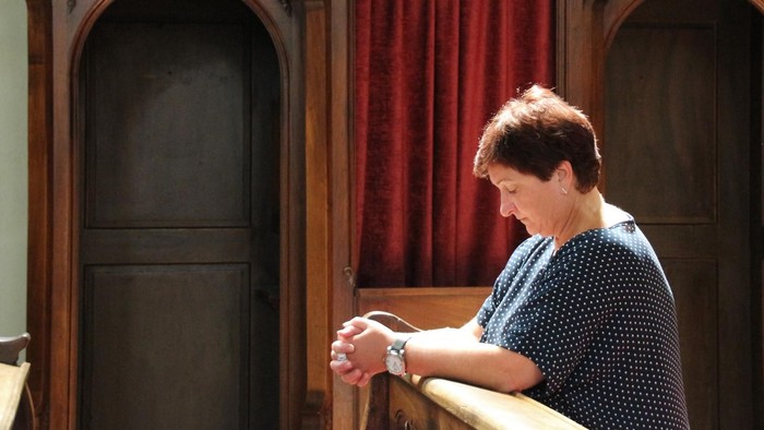 Frau kniet in einer Kirchenbank, die Hände zum Gebet gefaltet.