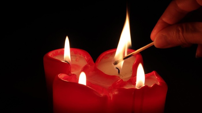 Eine Hand zündet mit einem Streichholz eine rote Kerze an.