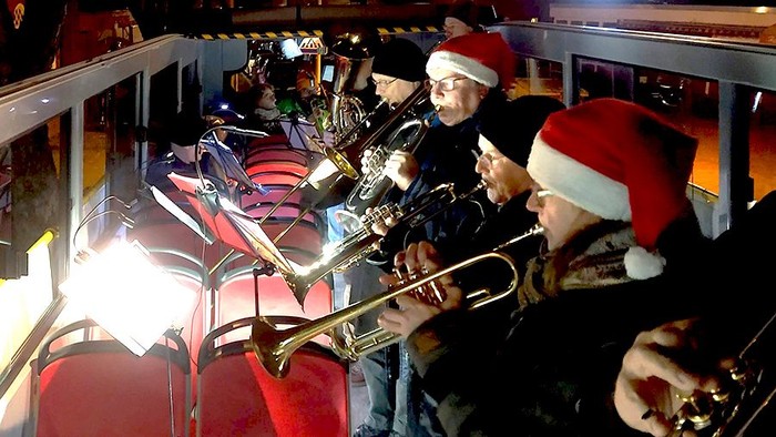 Blasmusiker mit Weihnachtsmützen spielen oben in einem Cabriobus.