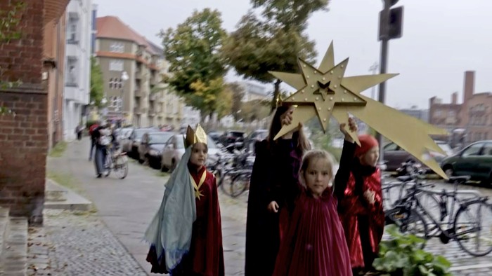 Kinder in Kostümen ziehen mit einem Stern durch die Stadt.