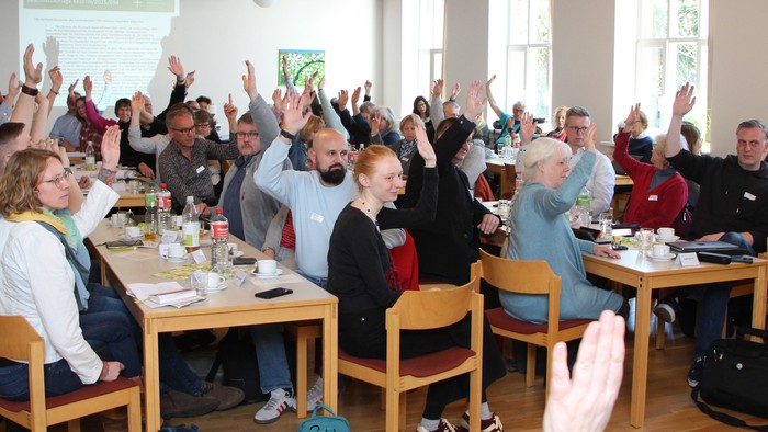 Ein großer Raum mit vielen Menschen an Tischen, die aufstehen und klatschen.