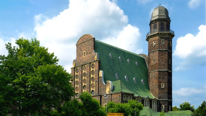 Große Backsteinkirche mit grünem Dach und hohem Turm unter blauem Himmel.