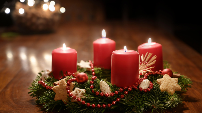 Vier brennende rote Kerzen, umgeben von Weihnachtsdekorationen auf einem Holztisch.