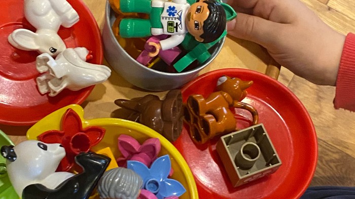 Kinderhände halten bunte Spielzeugschalen mit verschiedenen kleinen Spielzeugen und Figuren.