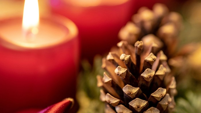 Drei brennende rote Kerzen mit Tannenzapfen und Grün.