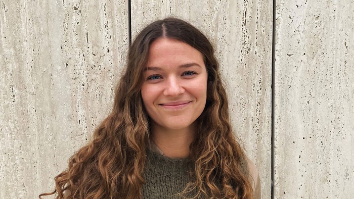 Ung kvinde med krøllet hår, der smiler op ad en betonvæg.