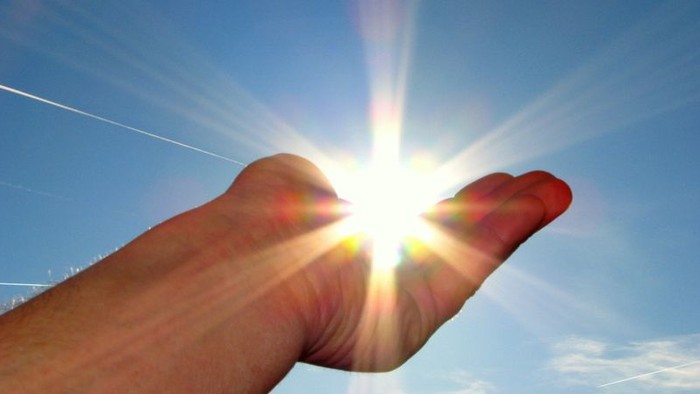 Eine Hand hält die Sonne am klaren Himmel