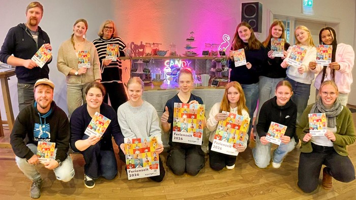 Vierzehn Jugendliche und Erwachsene in zwei Reihen halten Plakate und Hefte mit der Aufschrift