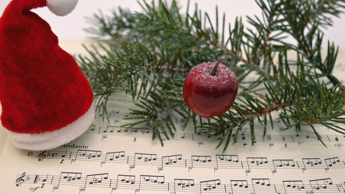 Ein roter Weihnachtsmannhut, ein glitzernder Apfel und Tannenzweige auf Notenblatt