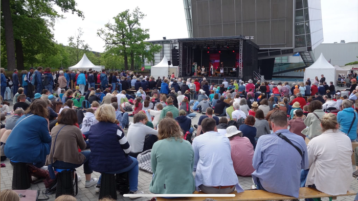 Großes Open-Air-Konzert mit Publikum auf Decken und Stühlen, Bühne mit Künstlern im Hintergrund.