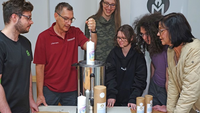 Sebastian Albinski, Ausbilder Jörg Ittermann, Tore Busch, Celia Hilkhausen, Serhat Kocaaslan und Geschäftsbereichsleiterin Sabine Riddermann zeigen einen Arbeitsschritt der Kerzenproduktion.